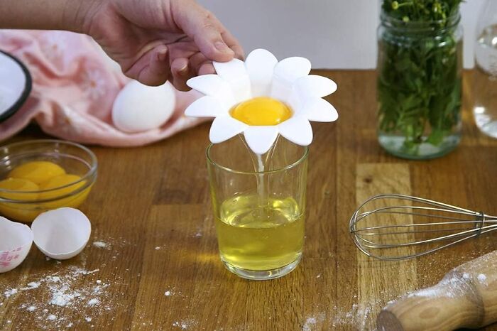 Egg separator from Peleg Design Shop used over a glass, surrounded by kitchen items.