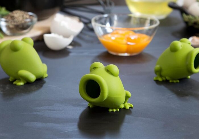 Green frog-shaped kitchen gadgets by Peleg Design Shop on a countertop with eggs and yolk in the background.