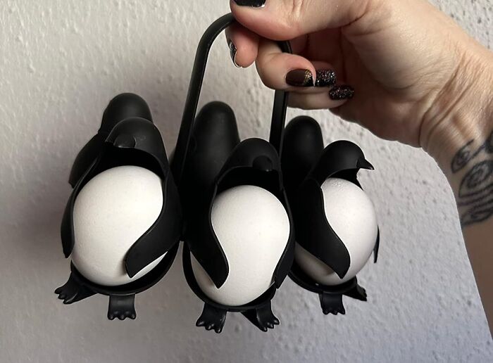 Penguin-shaped egg holders by Peleg Design Shop, held by a hand, showcasing playful kitchen accessories.
