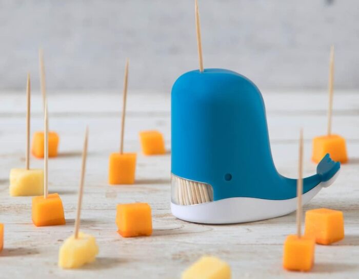 Whale-shaped toothpick holder from Peleg Design Shop surrounded by cheese cubes on wooden table.