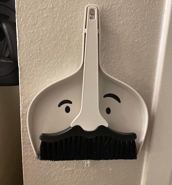 Whimsical Peleg Design dustpan and broom set with a face and mustache hanging on a wall.