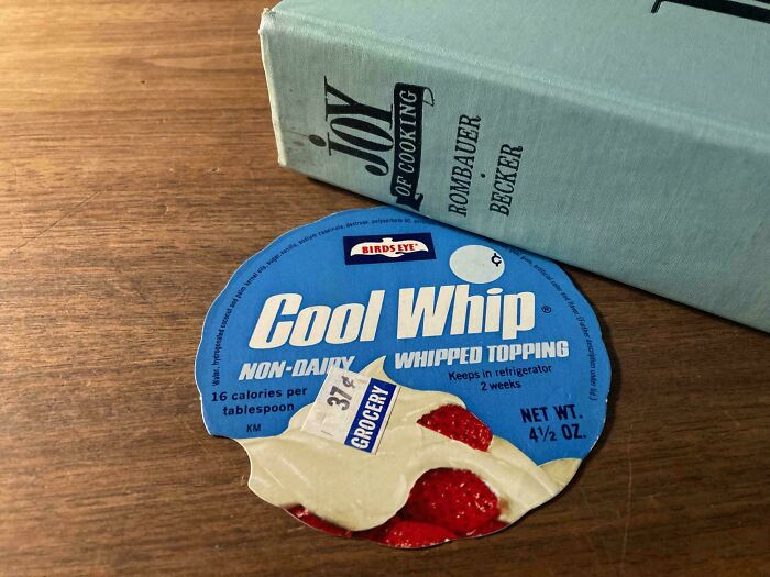 A Cool Whip lid used as a bookmark next to a cookbook, highlighting creative bookmarks by book lovers.