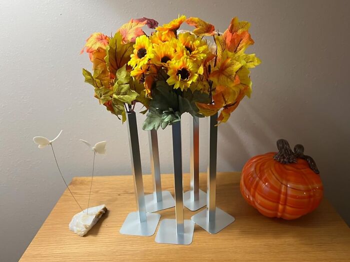 Autumn floral arrangement in silver vases from Peleg Design Shop, accompanied by a decorative orange pumpkin on a wooden table.