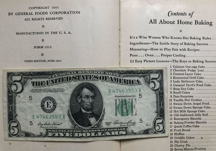Five-dollar bill used as a bookmark in an old baking recipe book, showcasing a creative find by book lovers.