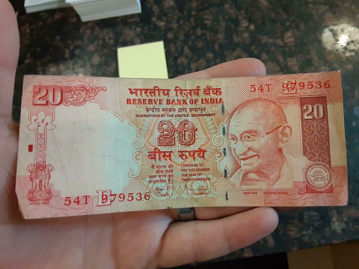 A 20 Rupee Indian banknote used as a unique bookmark held in a person's hand.