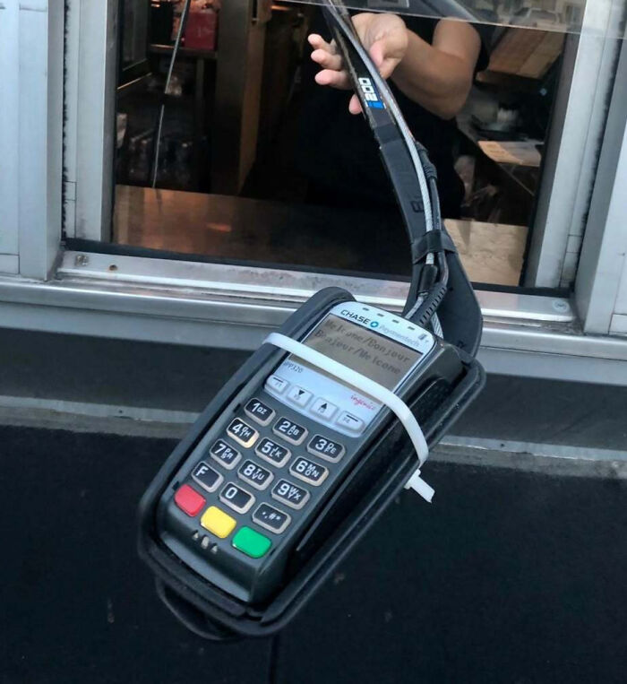 Contactless payment machine attached to a hockey stick used at a drive-thru, a unique scene in Canada.