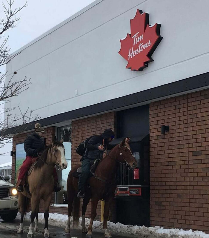 Two people on horseback using the Tim Hortons drive-thru in winter snow, a unique Canadian moment.