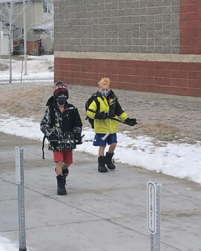 Two kids walking in snow wearing shorts and winter gear, embodying Canada things.