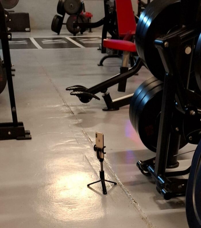 Smartphone on a tripod in a gym next to weightlifting equipment, capturing entitled behavior of gym users.