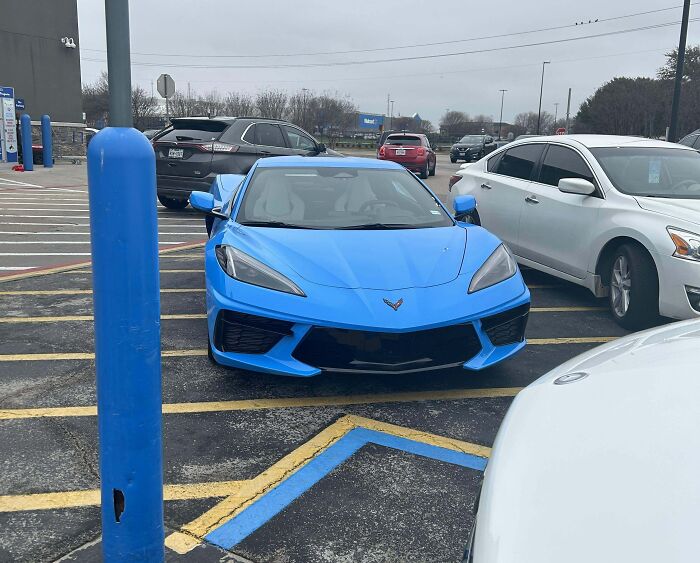 Blue sports car improperly parked across handicap space lines, showcasing entitled behavior.