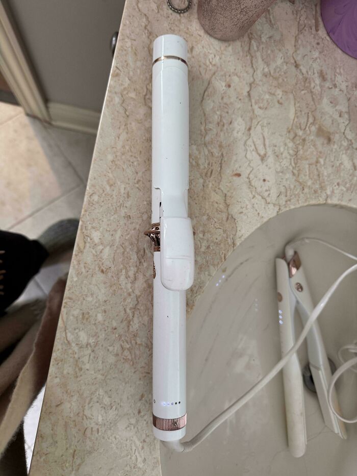 Curling iron placed near a sink on a bathroom counter, highlighting a design fail.