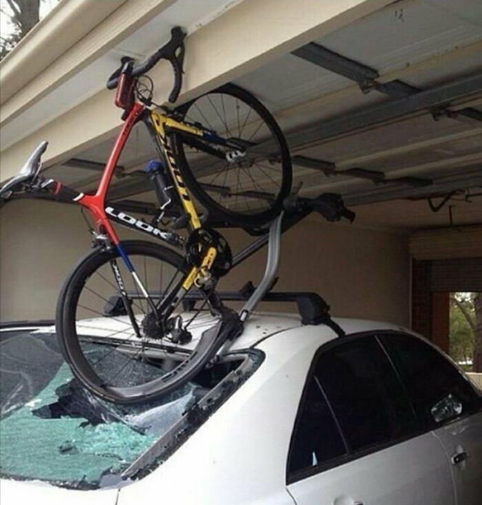 Car with a smashed windshield and a bicycle stuck in a garage accident, illustrating an expensive mishap.