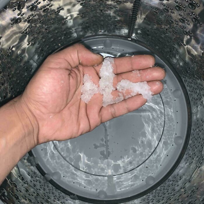 Hand holding detergent pieces in washing machine, showcasing results of an expensive accident.