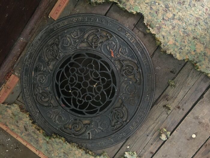 Ornate metal grate uncovered during home-discovery-finds, surrounded by worn wood and carpet remnants.