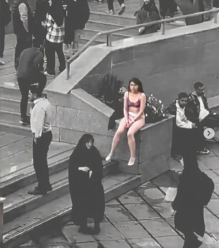 A woman in colorful clothing contrasts with a grayscale crowd in a historical setting.