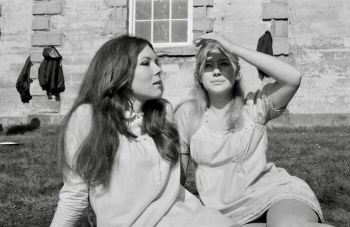 Two women sitting on grass beside a historic building, capturing forgotten corners of history.