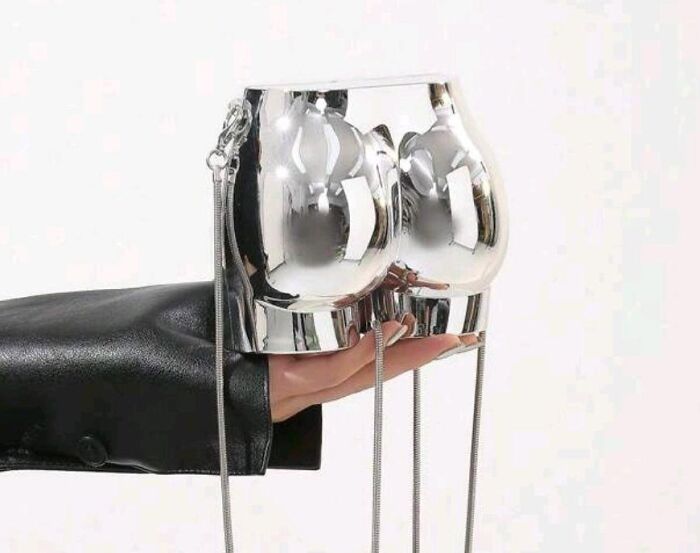 Fashion disaster: hand holding silver metal bag shaped like shorts, reflecting light.