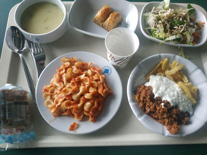 Comida cotidiana variada en bandeja, incluye pasta, ensalada y postre dulce.