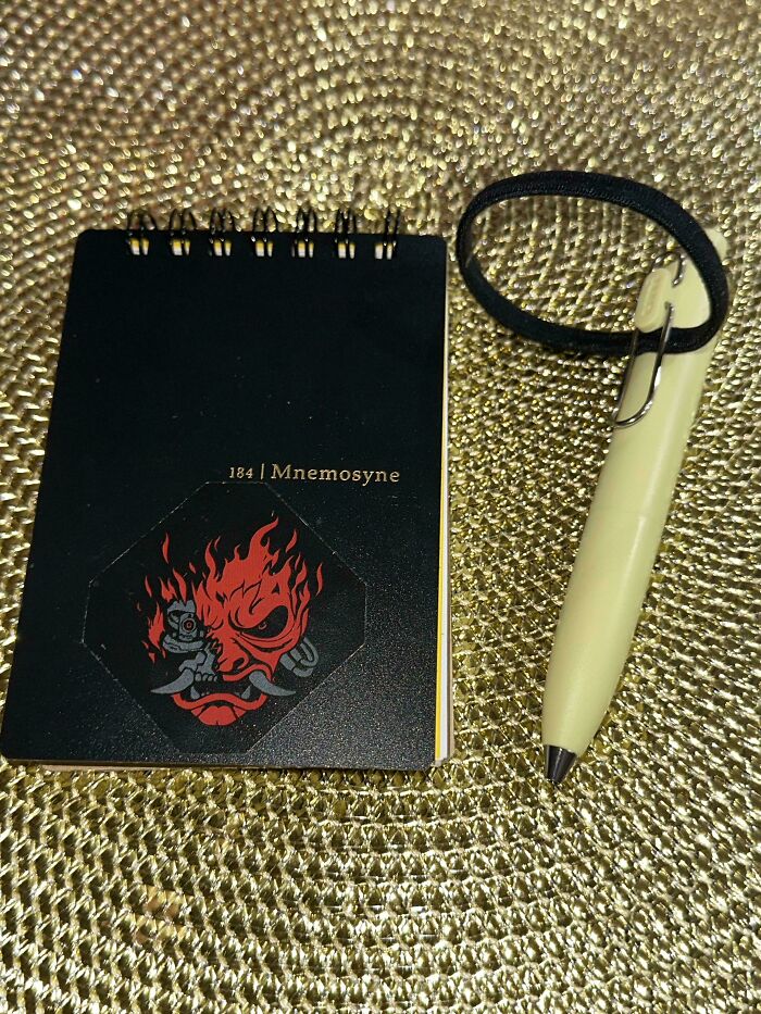 Black spiral notebook with a red mask design and a beige pen on a textured gold surface, representing dads parenting moments.