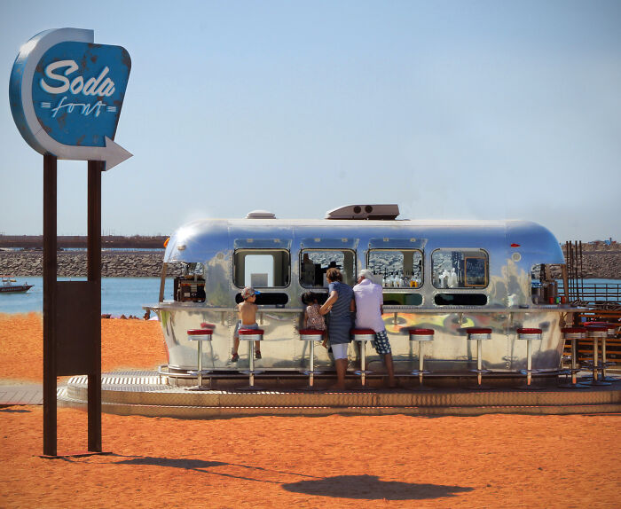 Retro soda trailer on a Dubai beach with people enjoying drinks, featuring a metallic finish and vibrant red stools.