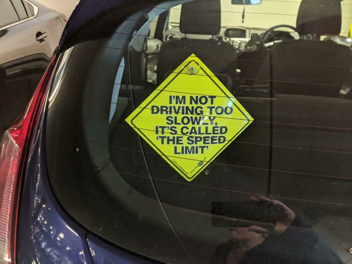 Car window sticker humorously displays passive-aggressive message about driving at the speed limit.