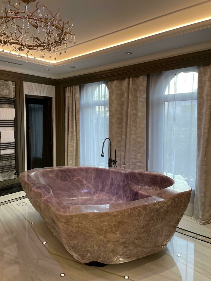 Luxurious stone bathtub in an elegant Dubai bathroom with a unique chandelier and tall windows.