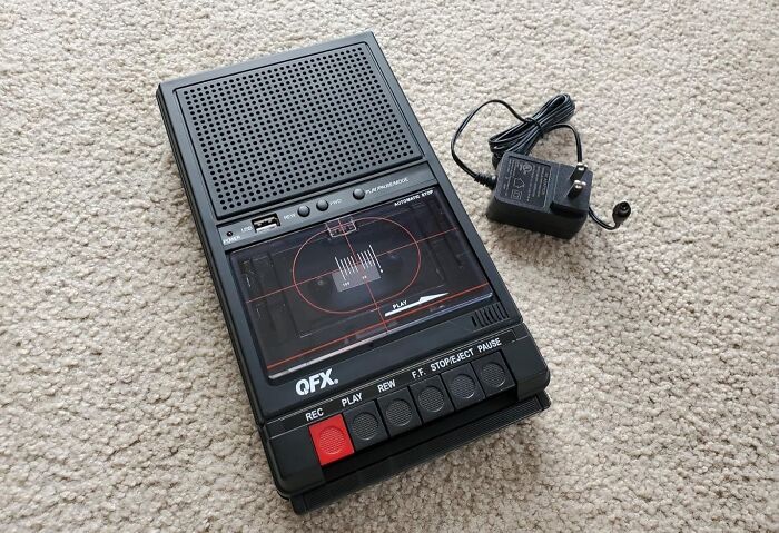 90s kids nostalgia: black cassette recorder with power adapter on beige carpet.