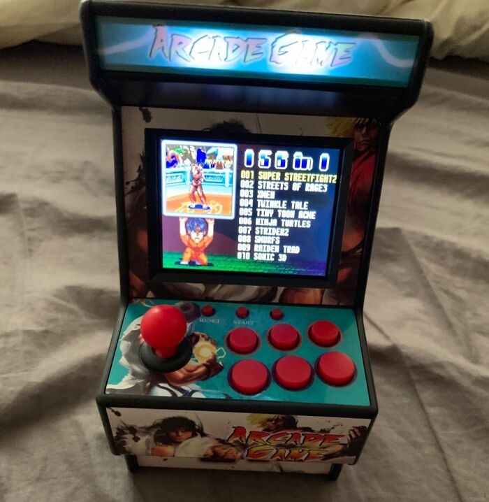 Mini arcade game machine with screen displaying classic 90s games, featuring joystick and red buttons.