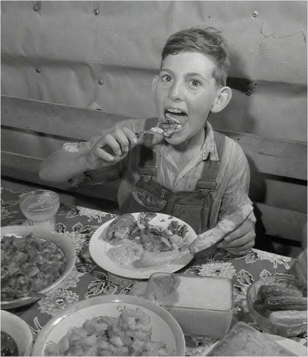 A historical photo of a boy in overalls enjoying a meal, showcasing past dining customs.