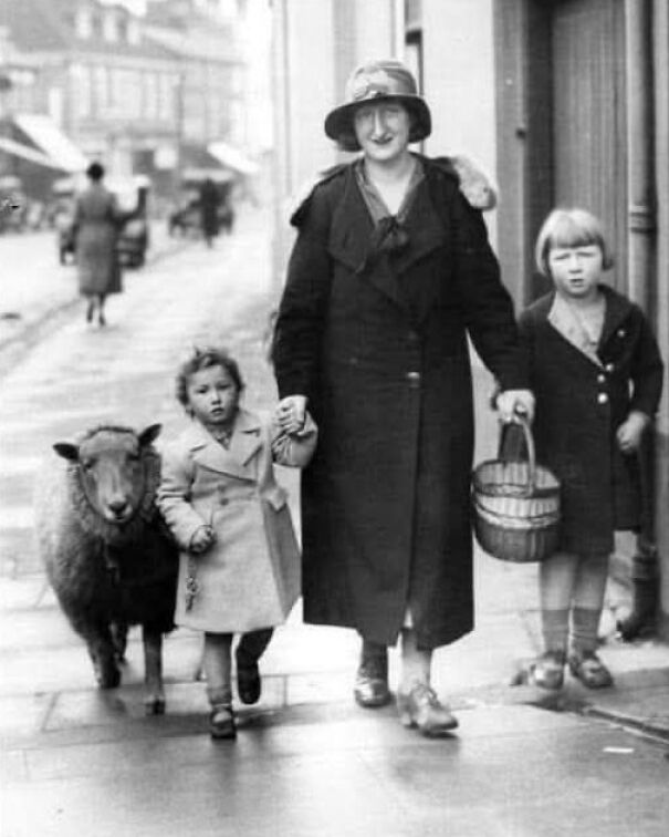 A woman with children walks a sheep down a historical street, showcasing an interesting perspective of the past.