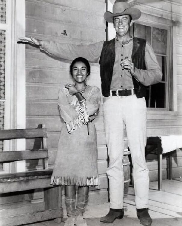 Vintage photo of a tall cowboy and shorter woman in traditional attire, showcasing a humorous height contrast.