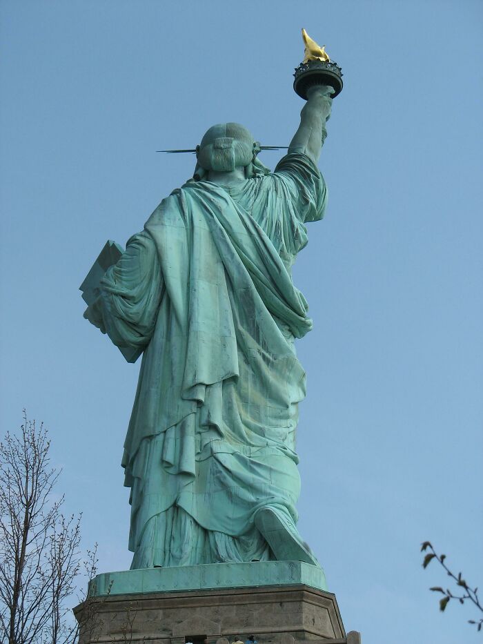 Rear view of the Statue of Liberty holding a torch, an iconic place in the world, under a clear blue sky.