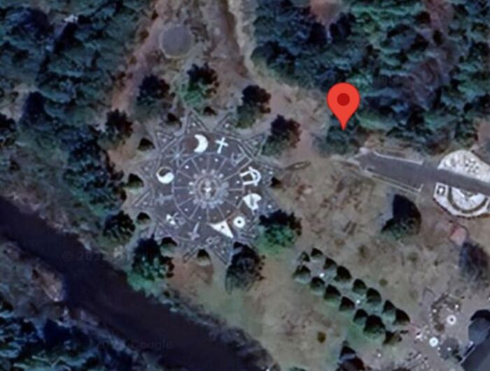 Strange circular pattern with symbols found on Google Earth, marked by a red pin in a forested area.