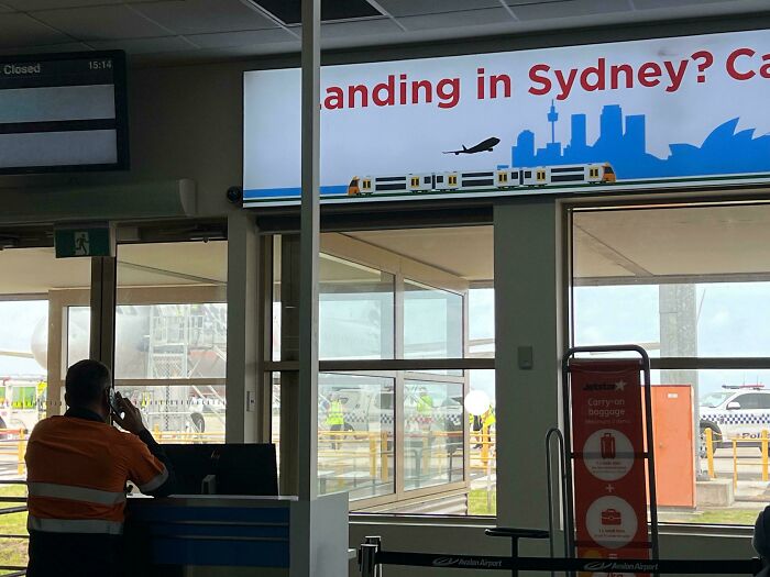 Sydney airport sign with skyline and public transport imagery, viewed from inside the terminal.
