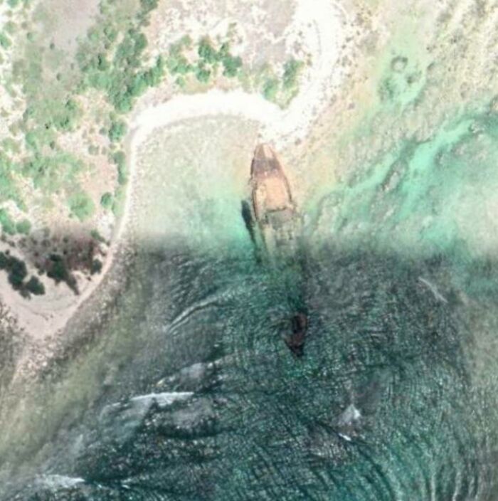 Aerial view of a shipwreck partially submerged in clear coastal waters, a strange sight found on Google Earth.