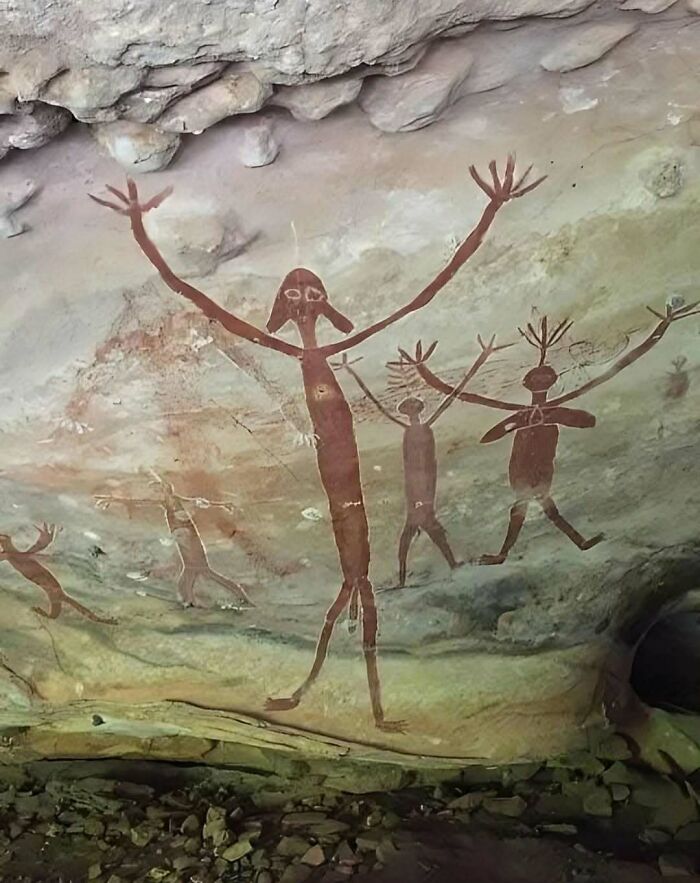 Ancient explorers' rock art depicting human figures with outstretched arms on a cave wall.