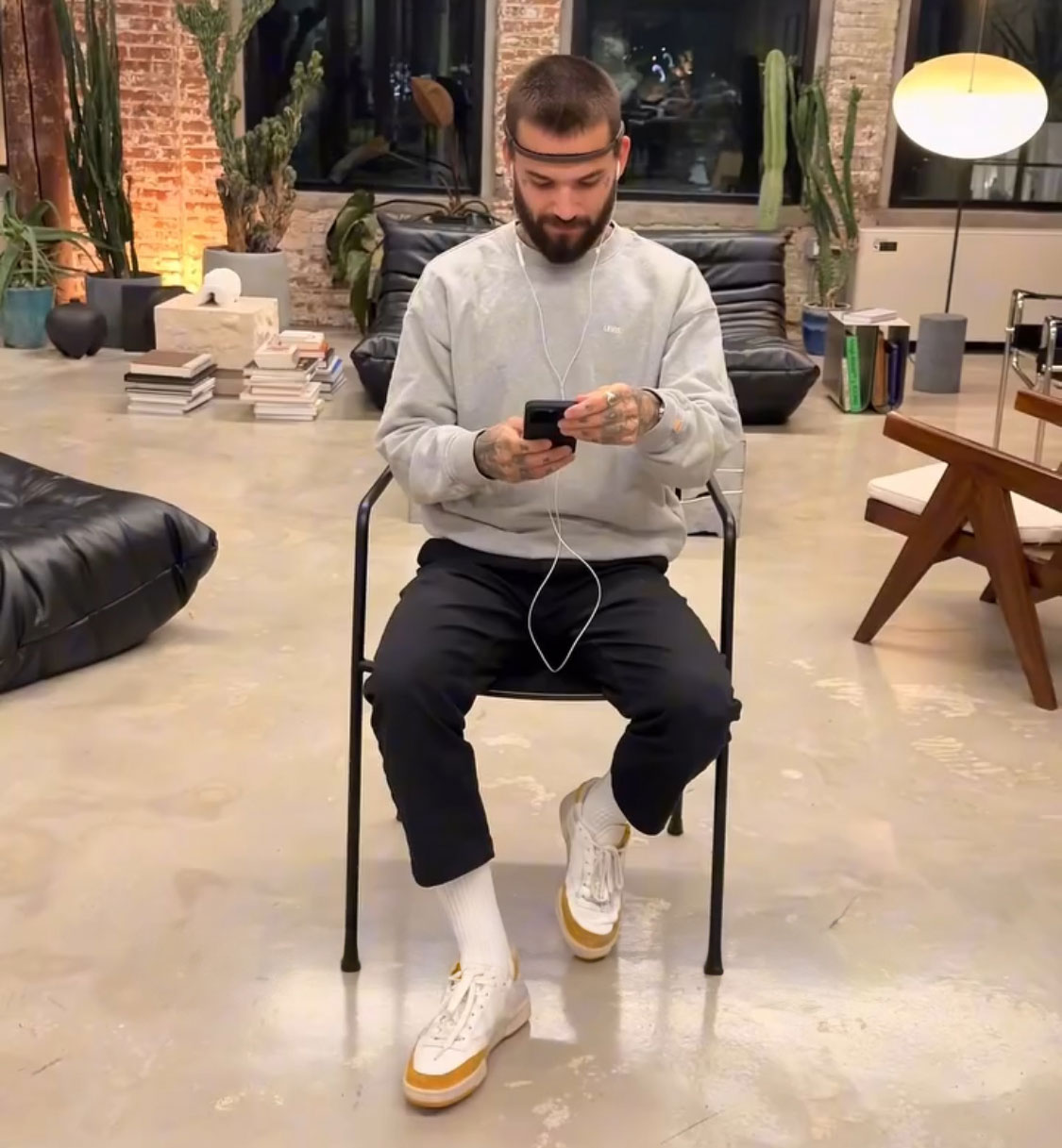 Man seated with brain activity headband, using a smartphone in a modern studio, exploring unique brain activity tattoo concept.