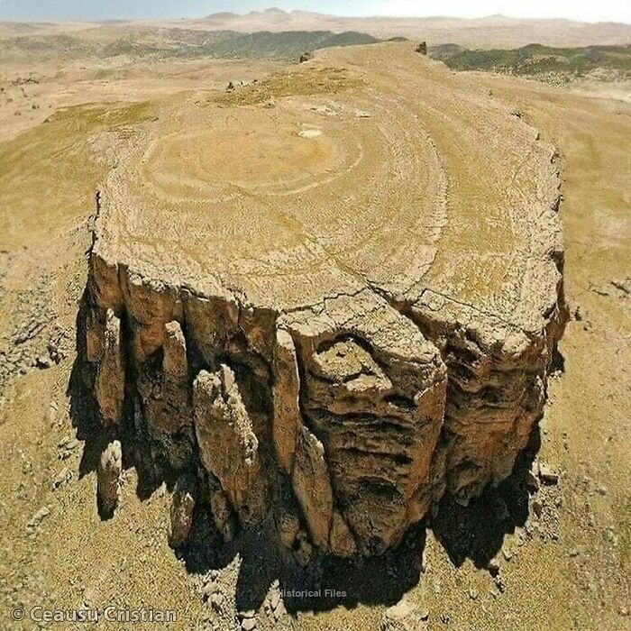Ancient cliff formation resembling a massive step pyramid in a desert landscape.