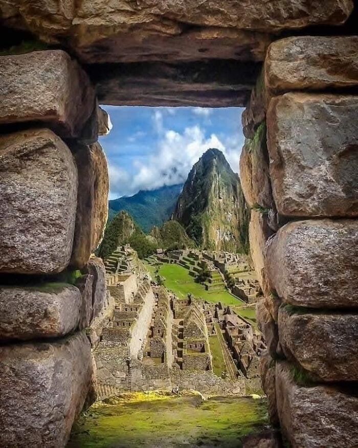 View of ancient ruins and mountains through stone archway.