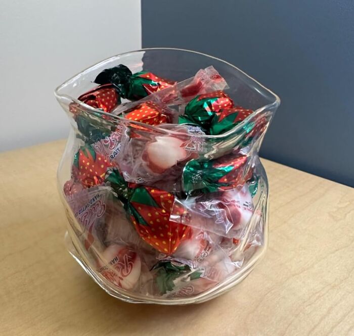 A glass jar filled with strawberry-wrapped candies by Genuine Fred on a wooden table.