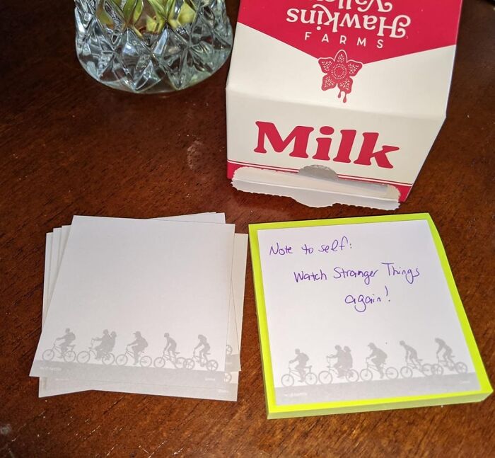 Genuine Fred sticky notes with a handwritten reminder next to an opened milk carton on a wooden surface.