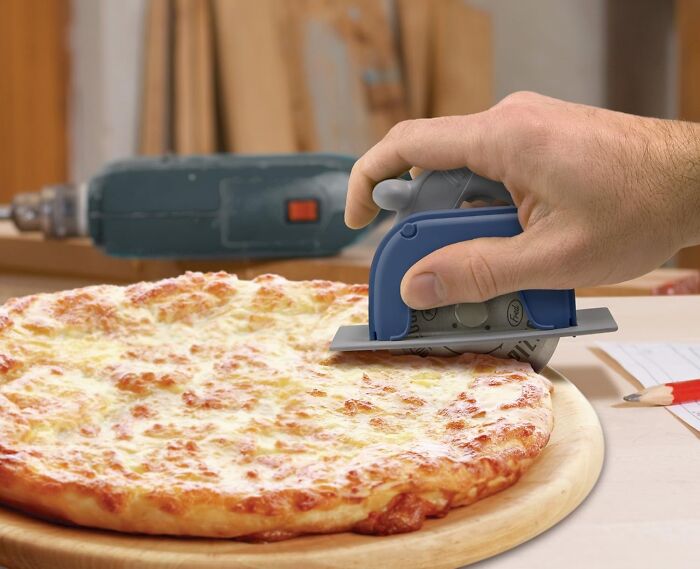 Genuine Fred circular saw pizza cutter in use on a cheese pizza on a wooden board.