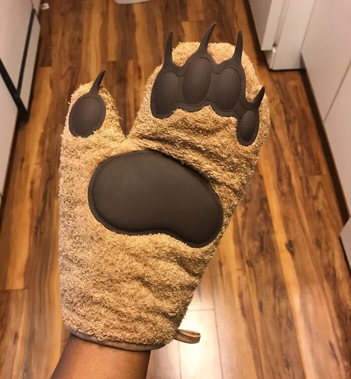 Genuine Fred bear paw oven mitt held up, showcasing its playful design against a wooden kitchen floor.