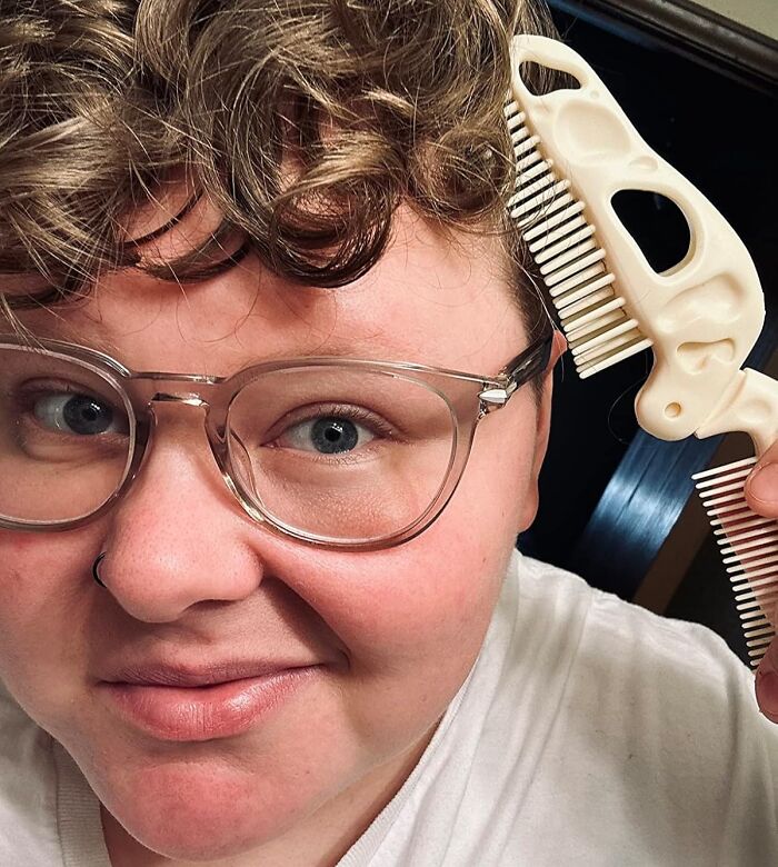 Person with glasses using a Genuine Fred comb on curly hair, smiling at the camera.