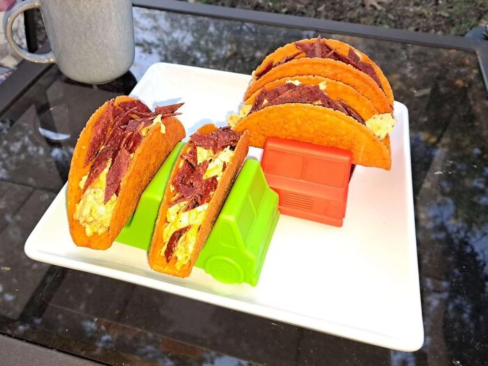 Tacos served in colorful truck holders by Genuine Fred on a white plate outdoors.