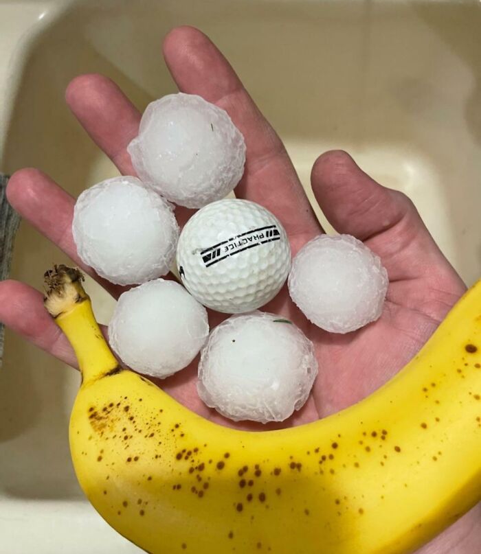 Hand holding large hailstones and a golf ball, with a banana for scale, showcasing nature's power.