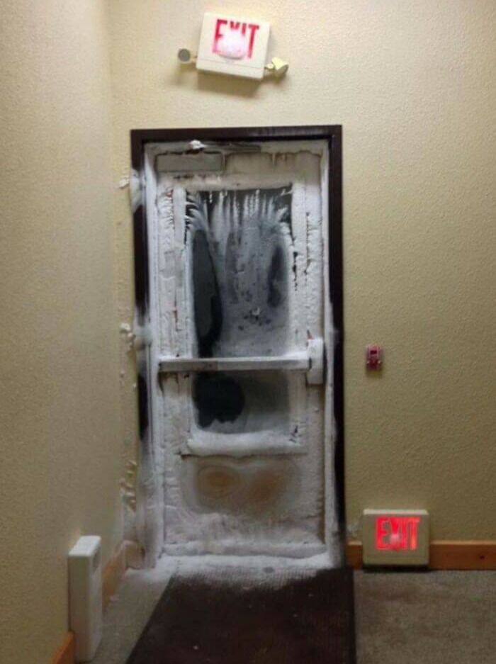 Frozen door in hallway with exit sign, illustrating nature's powerful and terrifying winter force.