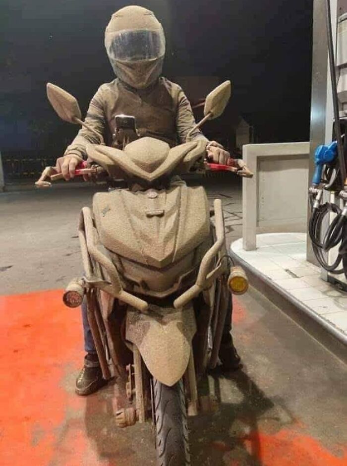 Rider on a mud-covered motorcycle at a gas station, showcasing nature’s powerful impact.
