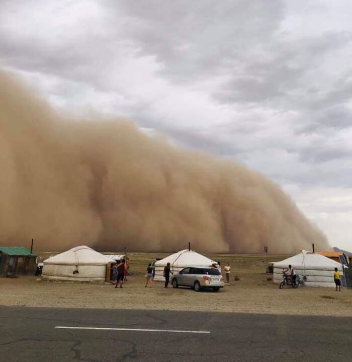 A massive sandstorm approaches yurts, showcasing nature's powerful and terrifying force.