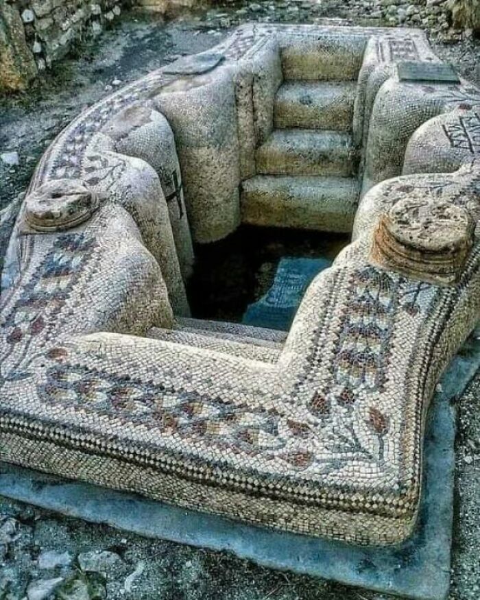 Ancient mosaic bath with intricate designs, featuring preserved historical artwork and steps.